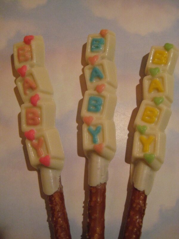 Three white chocolate-covered pretzel rods from the "24-Chocolate Covered Pretzel Rods-BABY Verse-Baby Shower Favors," each featuring pastel letters spelling "BABY" and tiny hearts.