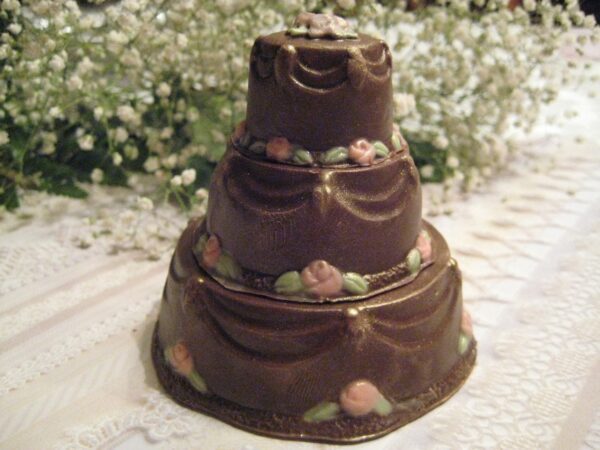A 12-Elegant Solid Chocolate Wedding Cake Favor features a three-tier design with decorative draping and pink floral accents, accompanied by delicate white flowers.