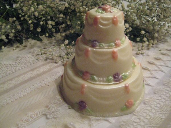 A three-tiered white cake adorned with small orange, purple flowers, and green leaves rests on a lace-covered table. It's the 12-Elegant Solid Chocolate Wedding Cake Favor.