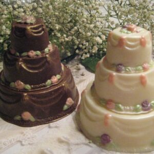 Two small Elegant Solid Chocolate Wedding Cake Favors, tiered and adorned with pastel flowers, are set on a lace tablecloth with white baby's breath in the background.