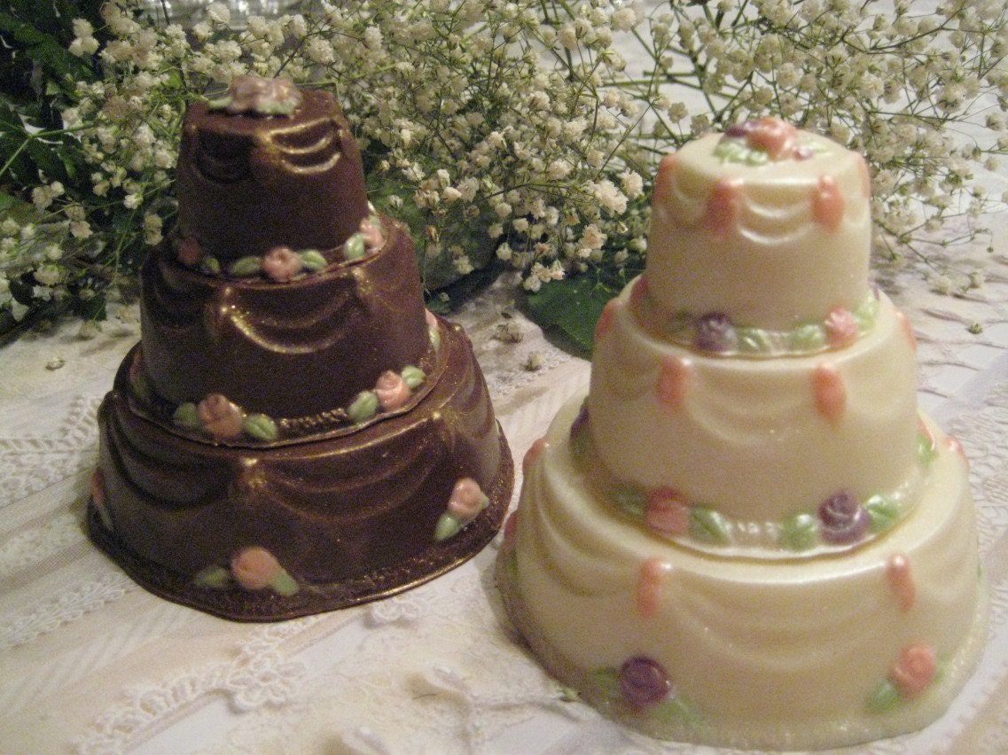 Two small Elegant Solid Chocolate Wedding Cake Favors, tiered and adorned with pastel flowers, are set on a lace tablecloth with white baby's breath in the background.