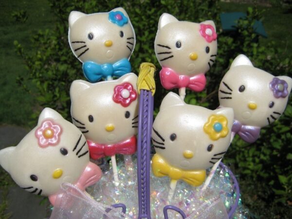 Displayed in a container are six white chocolate lollipop favors, shaped like cats with colorful bows and flowers, from the 12-Say Hello To My Sparkling Kitty Kat collection.
