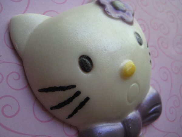 Close-up of a Hello Kitty face with a flower against a pink, swirling background, featured on the "12-Say Hello To My Sparkling Kitty Kat White Chocolate Lollipop Favors.