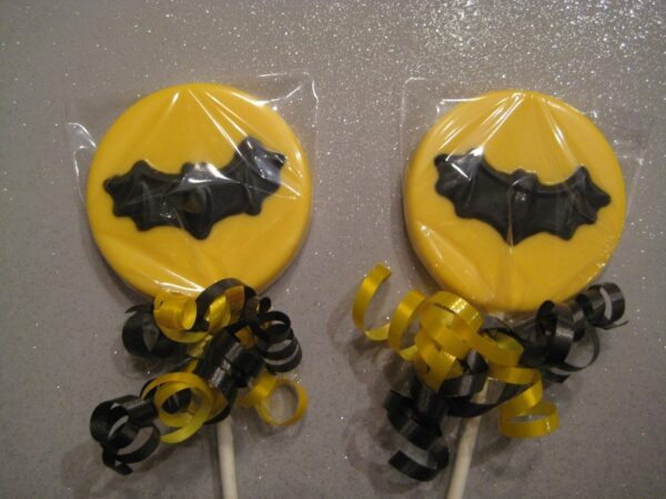 Two chocolate lollipops with black bat designs, wrapped in plastic and adorned with yellow and black curly ribbons.