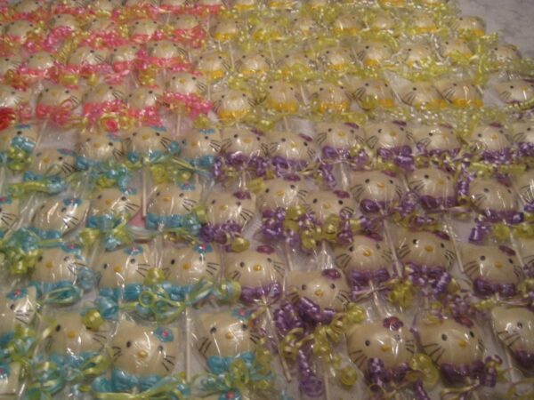 Rows of 12-Say Hello To My Sparkling Kitty Kat White Chocolate Lollipop Favors wrapped in colorful ribbons, arranged in pink, yellow, blue, and purple sections.