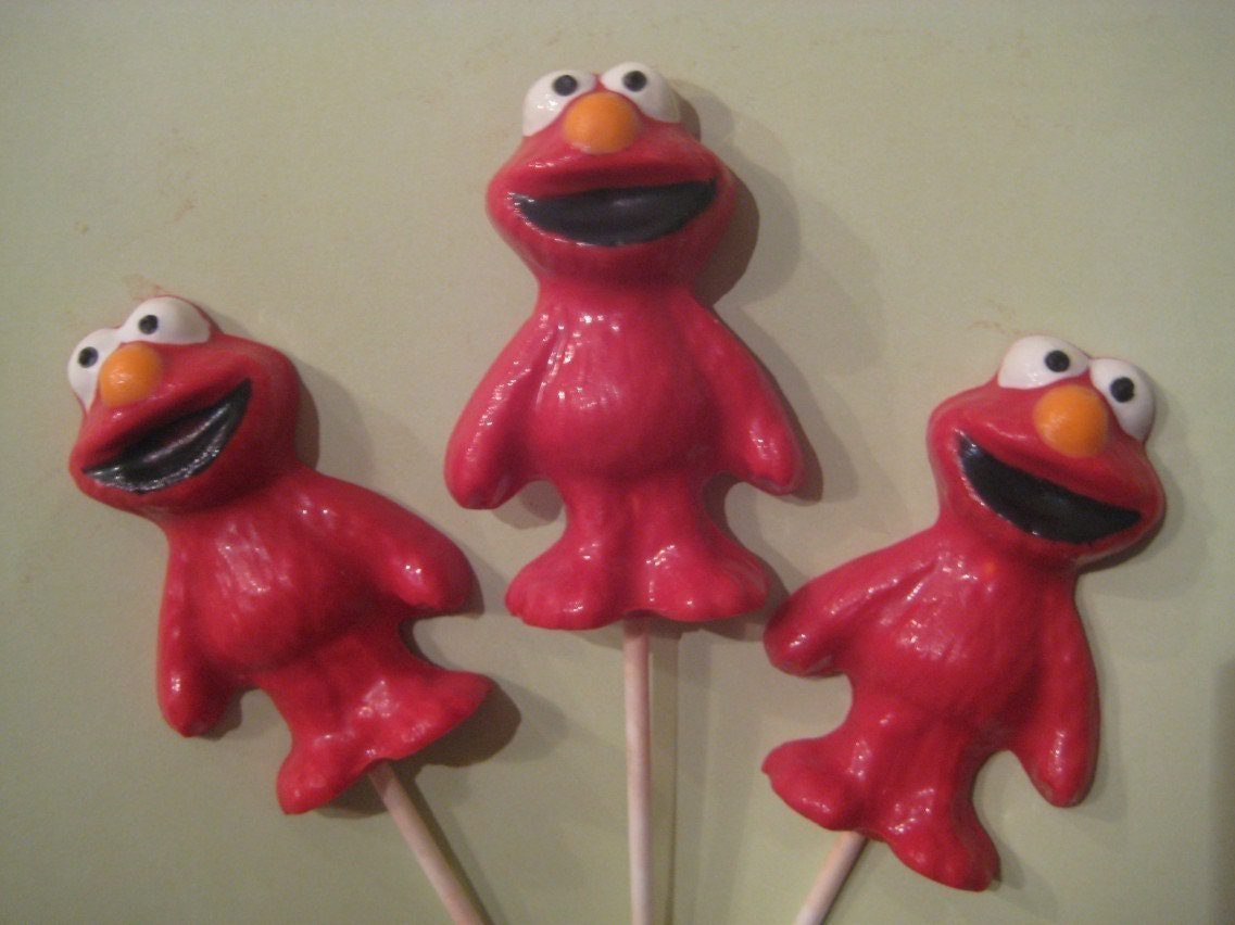 Three Elmo-shaped chocolate lollipops arranged on a light green background.