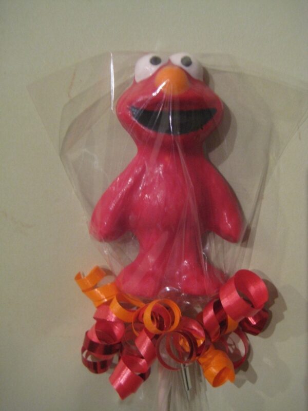 Red, character-shaped chocolate candy with big eyes, wrapped in clear plastic and adorned with red and orange curly ribbons at the base.