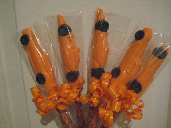 Race car-themed chocolate-dipped pretzel sticks decorated with black buttons, wrapped in clear plastic, and adorned with orange curly ribbons.