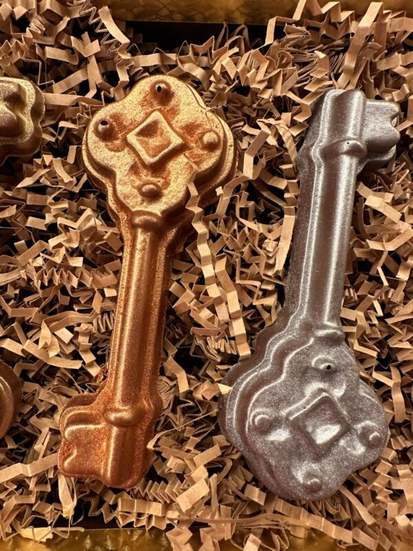 Four milk chocolate keys, including two gold, one bronze, and one silver, are presented in a gift box on crinkled brown paper.