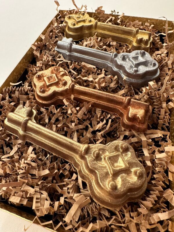 Four ornate milk chocolate keys—two gold, one bronze, and one silver—are showcased on crinkled paper in a gift box.