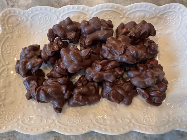 A 10-ounce serving of Decadent Dark Chocolate Covered Peanuts is stacked on a white ornate plate placed on a gray surface.