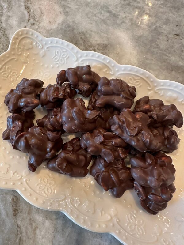 A plate of 10 Ounces of Decadent Dark Chocolate Covered Peanuts is placed on a marble surface.