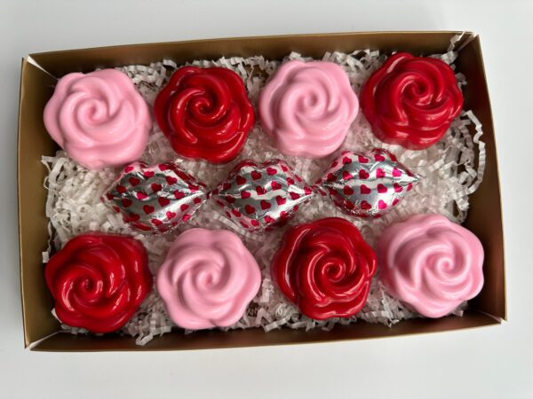 A box of Oreo chocolates shaped like roses, covered in red and pink chocolate, includes three heart-patterned foil-wrapped chocolates on a bed of white shredded paper.