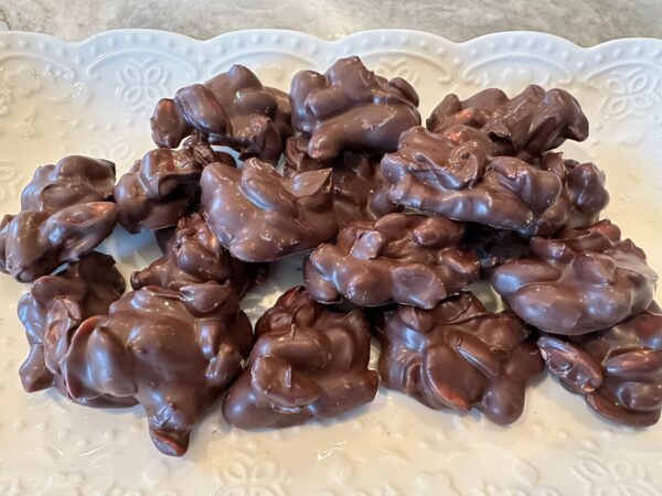 A decorative white platter holds a 10-ounce heap of Decadent Dark Chocolate Covered Peanuts.