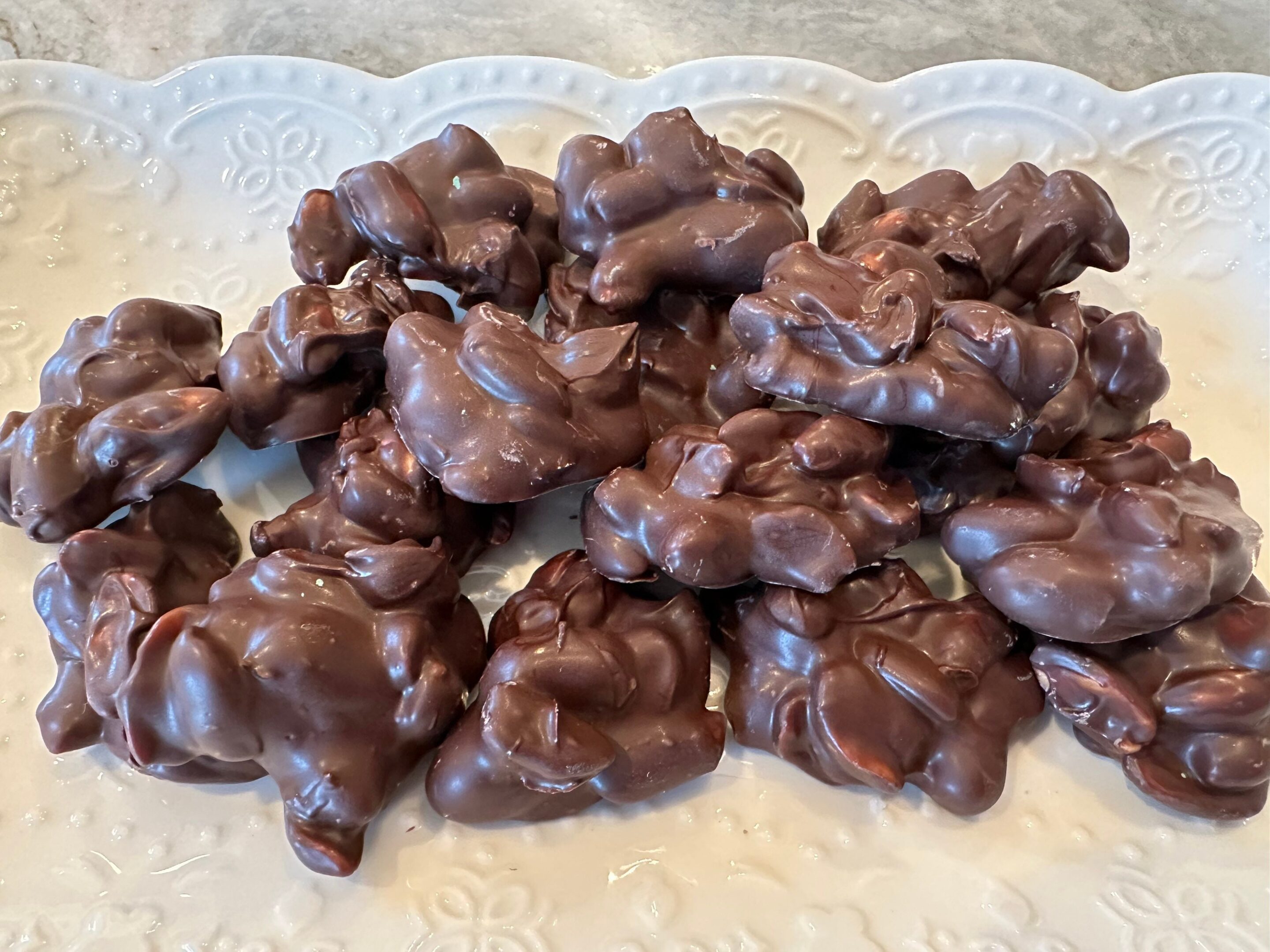 A decorative white platter holds a 10-ounce heap of Decadent Dark Chocolate Covered Peanuts.