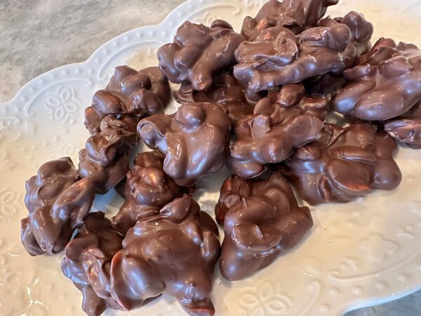 A white plate holds a pile of decadent dark chocolate covered peanuts, weighing 10 ounces, on a textured gray surface.