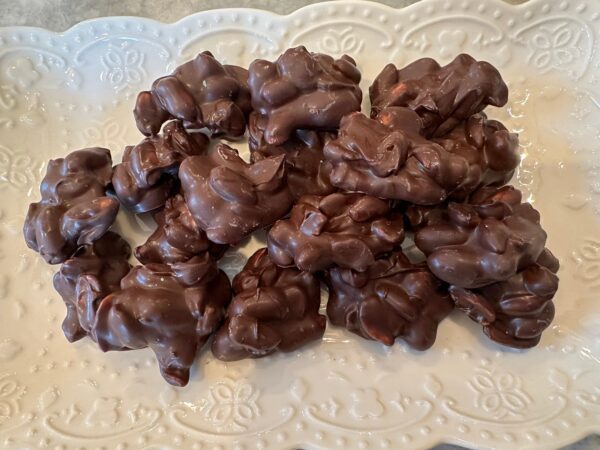 A decorative white plate displays multiple clusters of 10 ounces of decadent dark chocolate-covered peanuts.