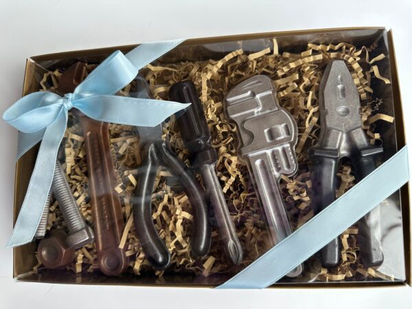 The 8 Piece Chocolate Tool Gift Set features chocolates shaped like a wrench, pliers, screwdriver, pipe wrench, and more, elegantly wrapped with a light blue ribbon.