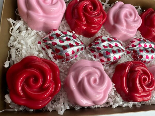 Box of pink and red chocolate-covered Oreo roses with heart-patterned foil, nestled on white shredded paper.