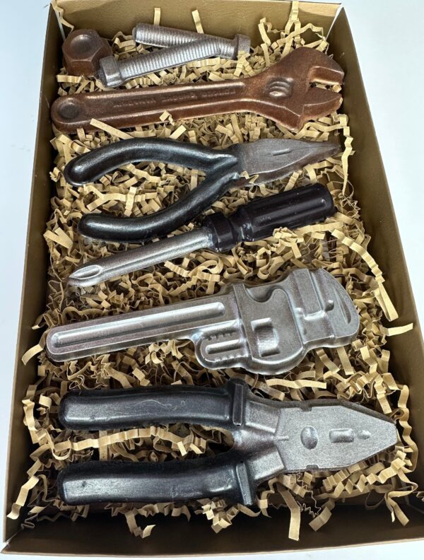 The 8 Piece Chocolate Tool Gift Set features a box of chocolate molded to resemble real tools like a wrench, pliers, screwdriver, and nuts and bolts, nestled in shredded paper filler.