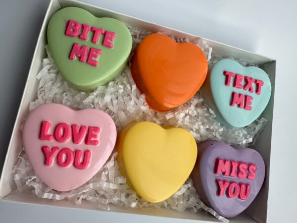 The 6 Conversation Heart Chocolate Covered Oreos Gift Box features heart-shaped cookies in pastel hues with messages like "Bite Me," "Text Me," "Love You," and "Miss You," beautifully arranged on white shredded paper.