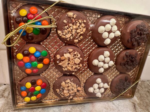 The "12-Chocolate Covered Oreo Cookies With Toppings Gift Box" features cookies topped with colorful candies, toffee pieces, white chocolate chips, and chocolate chips, all arranged in three rows and tied with a golden ribbon.
