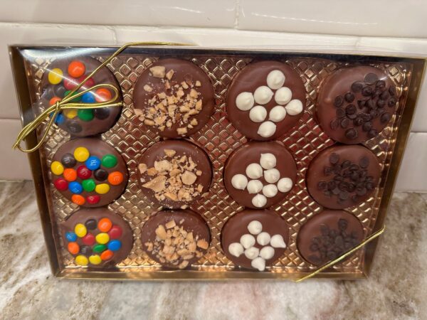 The 12-Chocolate Covered Oreo Cookies With Toppings Gift Box features a gold tray with twelve oreos, each adorned with unique toppings such as colorful candies, chopped nuts, mini marshmallows, and chocolate chips.