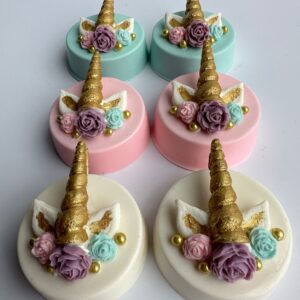Six unicorn-themed chocolate-covered Oreos with golden horns, adorned with roses, pastel colors, and edible pearls.