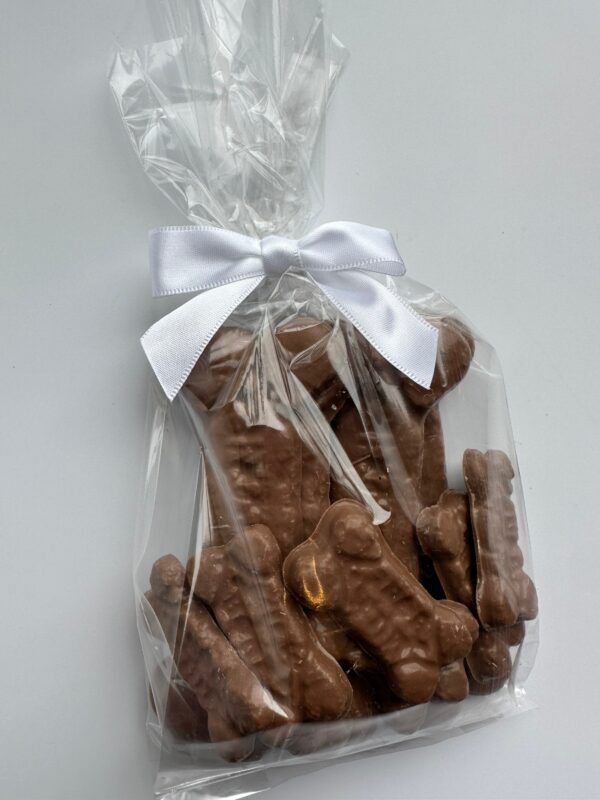 6 clear bags, each adorned with a white ribbon, contain chocolate dog bones perfect for birthdays or gag gifts.