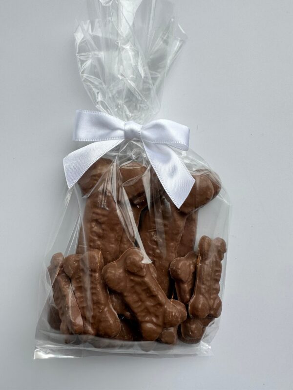A clear bag of "Chocolate Dog Bones" treats, shaped like bones and tied with a white ribbon, displayed on a plain background.