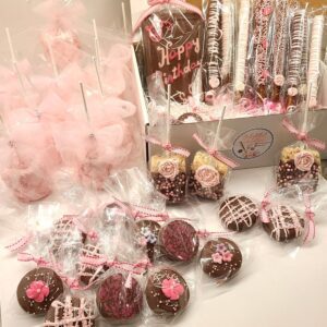 The Large Chocolate Treats Happy Birthday Box includes pink and brown themed birthday treats such as cake pops, pretzel rods, rice treats, and decorated cookies, all elegantly wrapped in clear bags with pink ribbons.