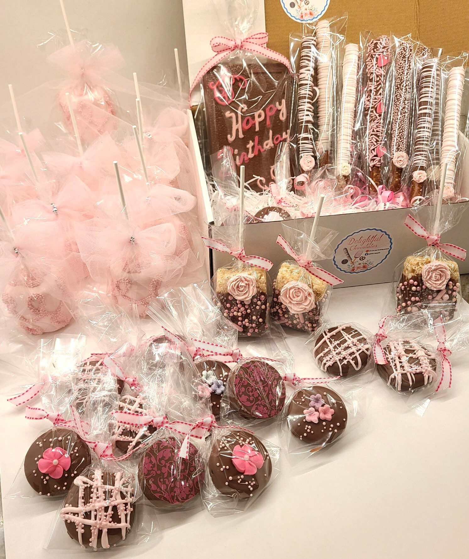 The Large Chocolate Treats Happy Birthday Box includes pink and brown themed birthday treats such as cake pops, pretzel rods, rice treats, and decorated cookies, all elegantly wrapped in clear bags with pink ribbons.