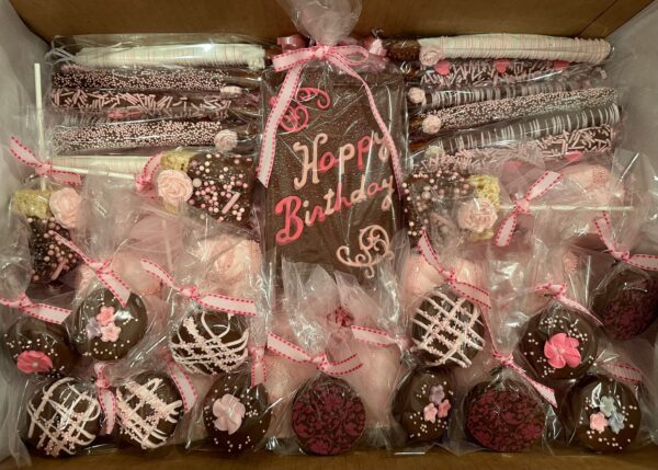 The Large Chocolate Treats Happy Birthday Box includes assorted chocolate-covered treats with pink decorations, featuring a large piece reading "Happy Birthday," all neatly arranged in a box.