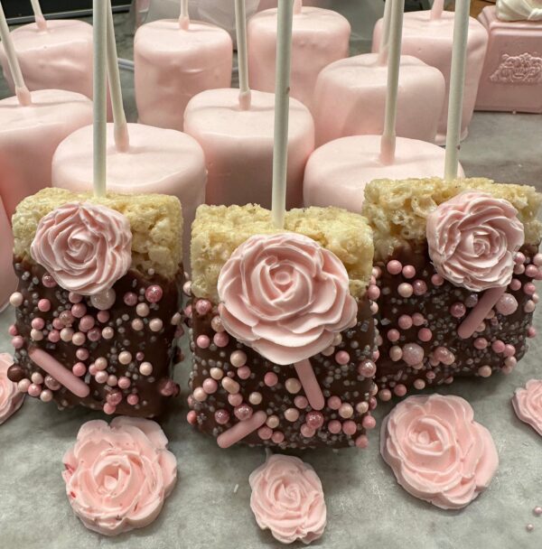 Pink-themed dessert pops include rice crispy treats and marshmallows with a chocolate coating, pink roses, and sprinkles. Product: 12 Chocolate Covered Rice Krispie Treats With Roses for Shower/Wedding/Birthday Party Favors.