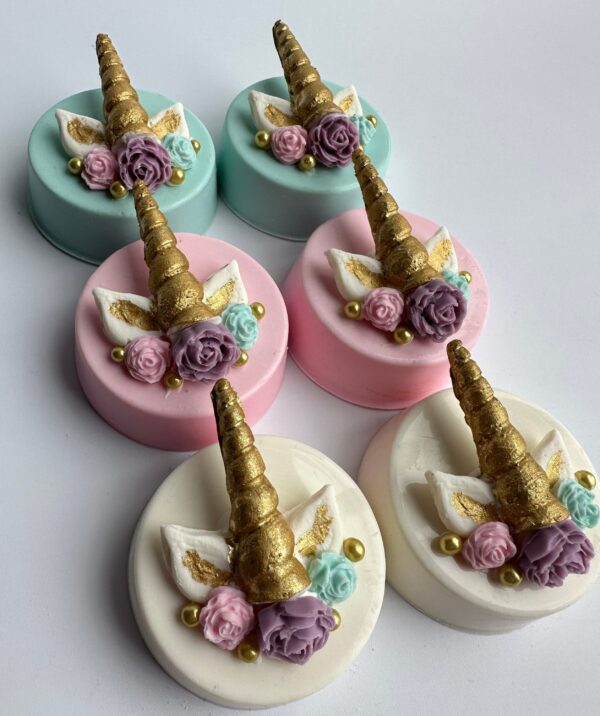 Unicorn-themed chocolate-covered Oreos with golden horns, flowers, and wings in pastel pink, blue, and white are arranged on a white surface. Perfect for birthdays, baby showers, or weddings.