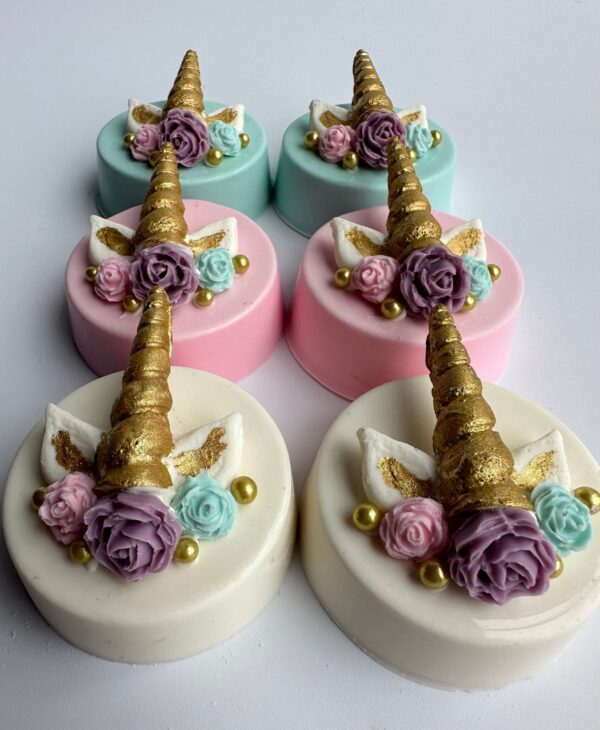 Two rows of six unicorn-themed cakes featuring gold horns, pastel flowers, and white wings on pink, white, and blue bases resemble the 12-unicorn chocolate-covered Oreos designed for birthday/baby shower/wedding celebrations.
