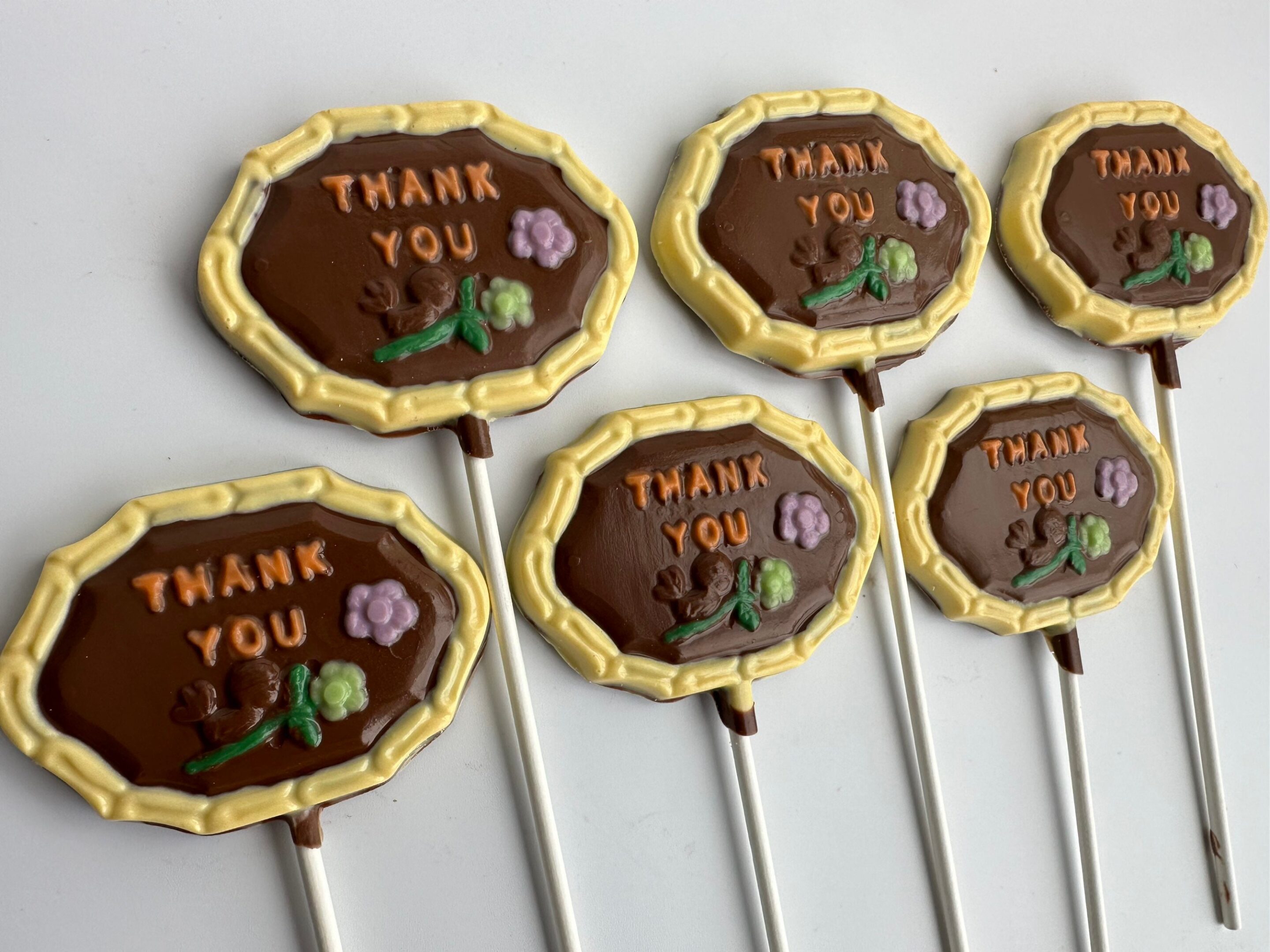 Five "Thank You" chocolate lollipops featuring colorful tree and flower designs on white sticks.