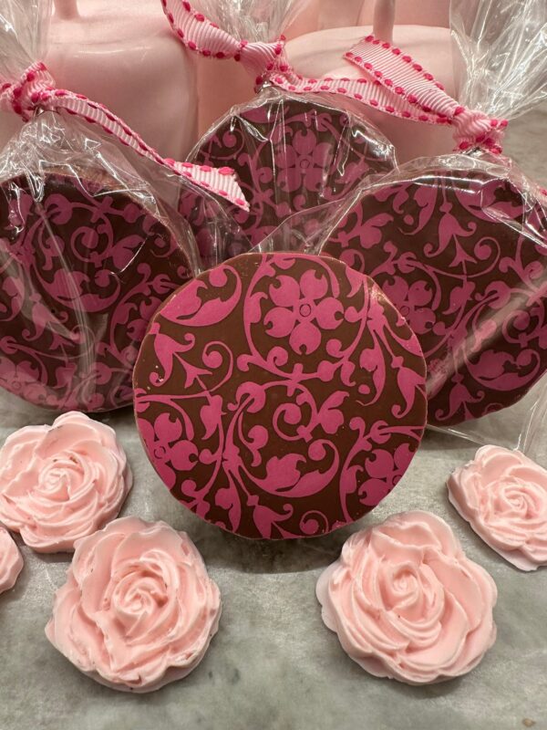 The Pink Floral Scroll Chocolate Covered Oreos come in a gift box featuring clear wrapping with bows, displaying pink and brown patterns, surrounded by rose-shaped confections. Perfect for weddings, birthdays, parties, or baby showers.