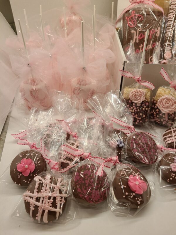The Large Chocolate Treats Happy Birthday Box features assorted chocolates wrapped in clear plastic and adorned with pink and white icing, ribbons, and flowers.