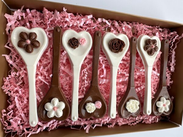 A box of six heart-shaped chocolate spoons with floral designs, set on pink paper shreds. Perfect as a Chocolate Heart Spoons Gift Box for Hot Chocolate, weddings, birthdays, or Mother's Day.