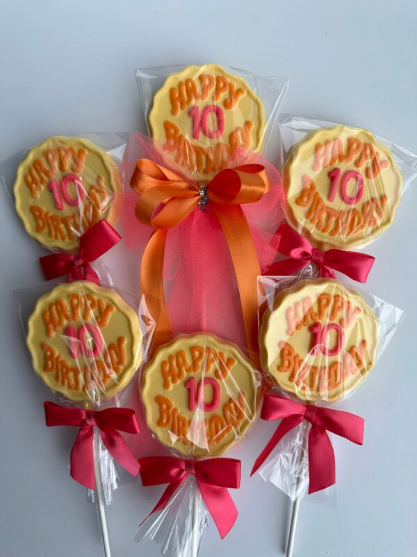 Six "Happy 10 Birthday" chocolate lollipops with yellow cookies, wrapped in plastic with red bows, and arranged in a fan shape around an orange and pink ribbon.