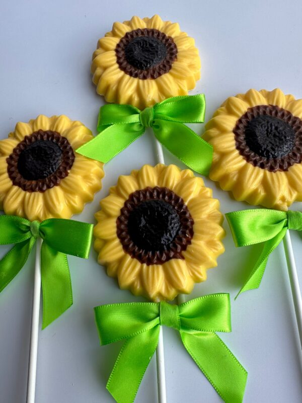 Four chocolate lollipops from the 24-Chocolate Sunflower Lollipops set, featuring yellow petals and brown centers with green ribbon ties, are displayed on a white surface.