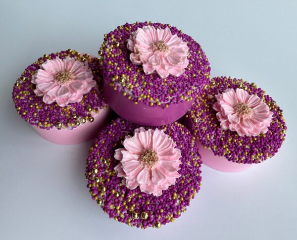 Four fuchsia and pink chocolate-covered Oreos, ideal for wedding, shower, or birthday favors, adorned with large pink flowers and surrounded by purple and gold sprinkles on a white background.
