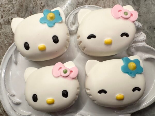 Four 12-Cute Kitty Chocolate Covered Oreo Favors with white coverings and pink and blue bows, displayed on a white tray.