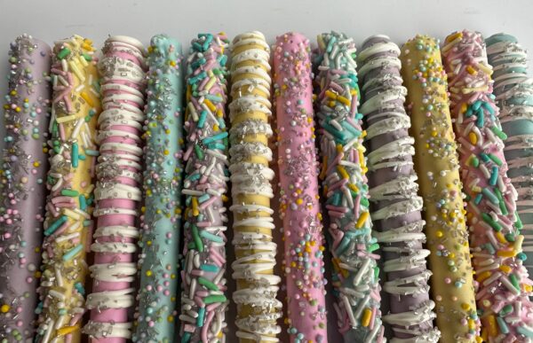 A row of Spring Decorated Chocolate Covered Pretzel Rods coated in pastel icing and assorted sprinkles.