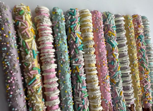 Spring Decorated Chocolate Covered Pretzel Rods feature colorful pretzel sticks coated in pastel chocolate and sprinkled with decorations, neatly arranged on a white background.
