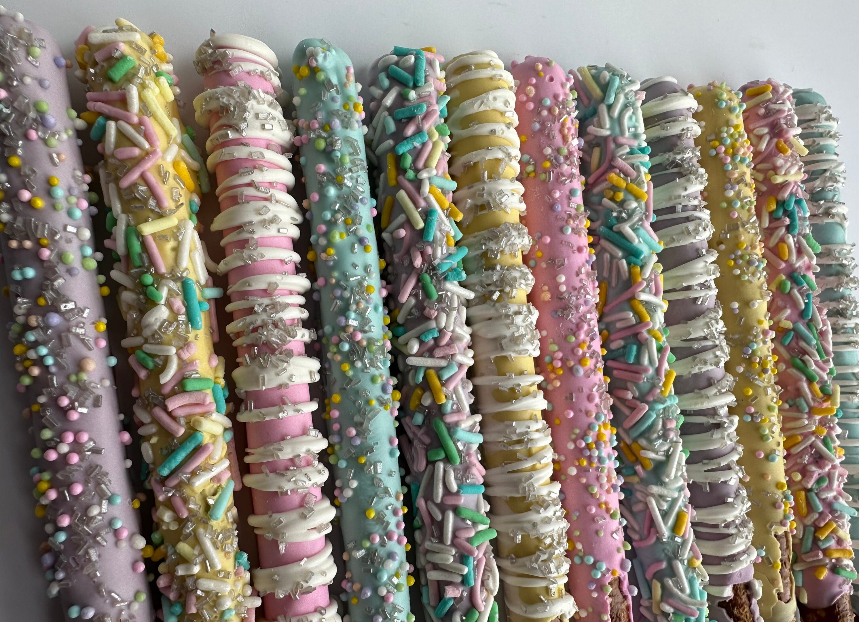 Spring Decorated Chocolate Covered Pretzel Rods feature colorful pretzel sticks coated in pastel chocolate and sprinkled with decorations, neatly arranged on a white background.