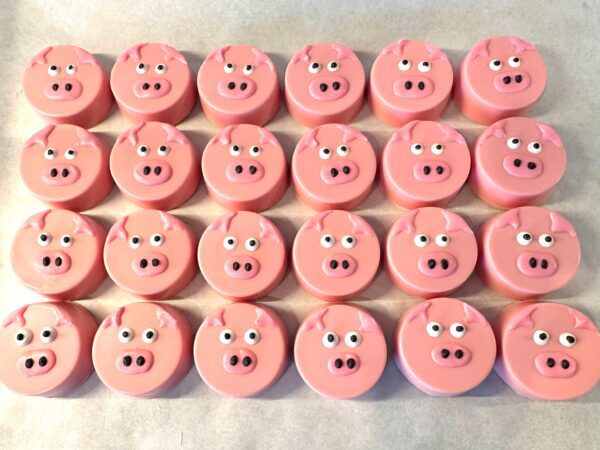 Twenty-four pink pig-faced Oreo favors are arranged in a grid on a white surface.