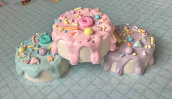 A set of 12 pastel-themed chocolate-covered Oreos featuring dripping icing and vibrant sprinkles is elegantly showcased on a light blue checkered tablecloth, ideal for birthdays or baby showers.