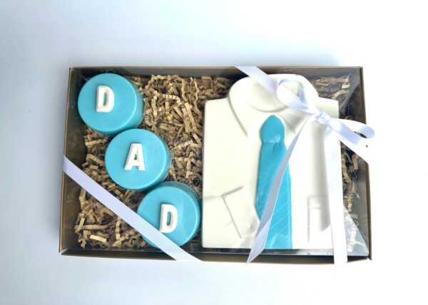 The DAD Chocolate Covered Oreo and White Chocolate Shirt Gift Box features cookies shaped like a shirt and tie, along with three round cookies spelling "DAD" in blue icing, all tied with a white ribbon.